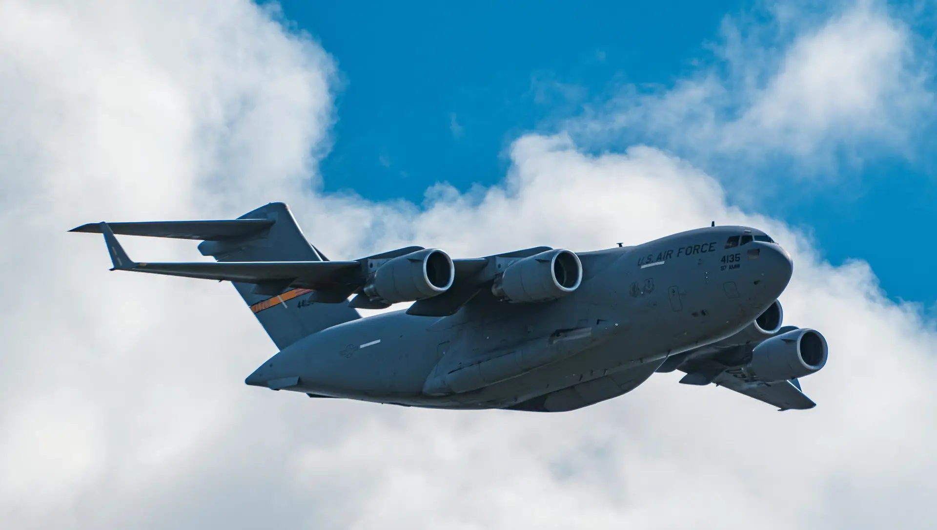 U.S. Air Force C-17 Globemaster III flying through cloudy sky on a clear day.